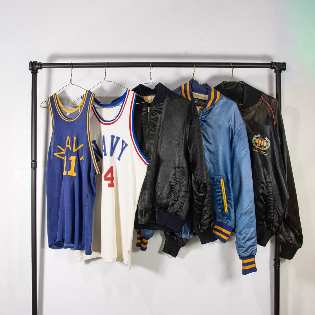 A group of vintage satin jackets and jerseys: A group of vintage satin jackets and jerseys, (2) "Navy" basketball jerseys sizes not labeled, (2) black jackets with military insignia and paraphernalia: small and xlarge, (1) "Navy" jacket size