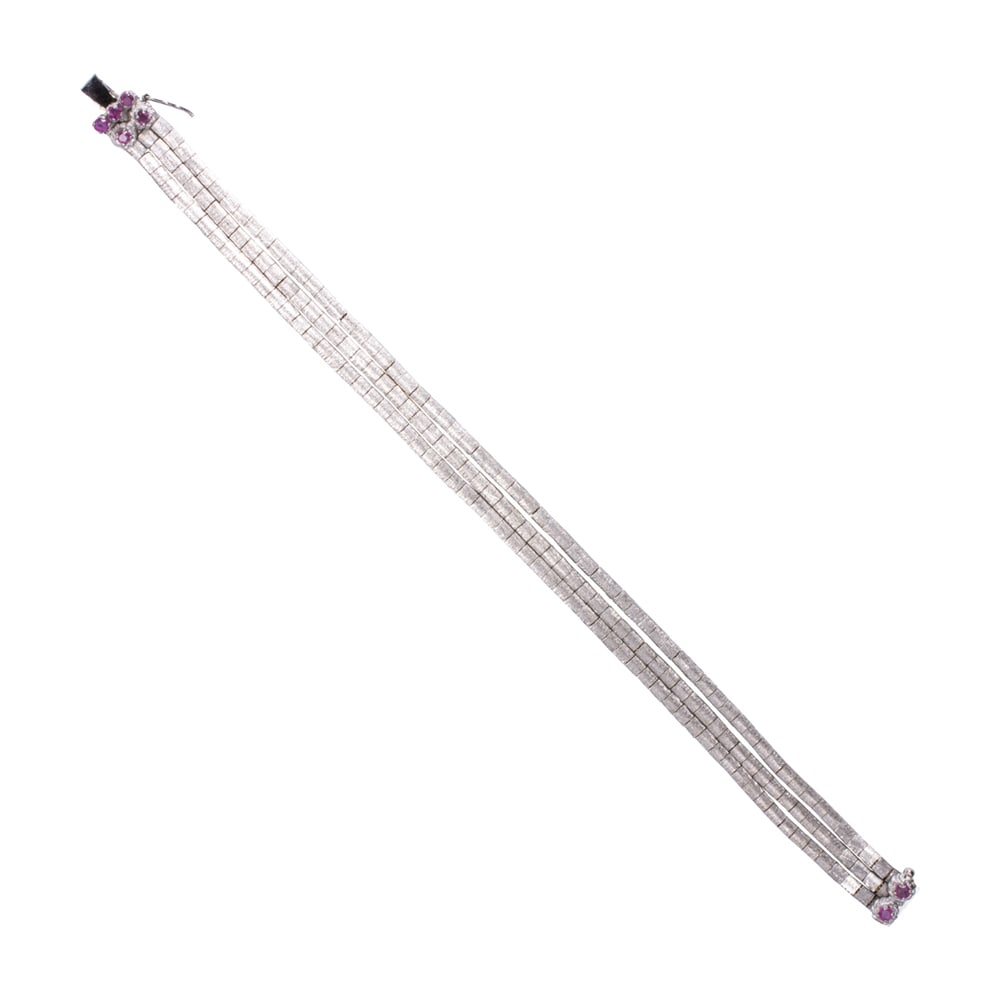 A ruby and 18k white gold bracelet: A ruby and 18k white gold bracelet Designed as a three strand textured omega chains joined by clasp set with seven round-cut rubies; length: 7 1/2 in; 22.40 grams