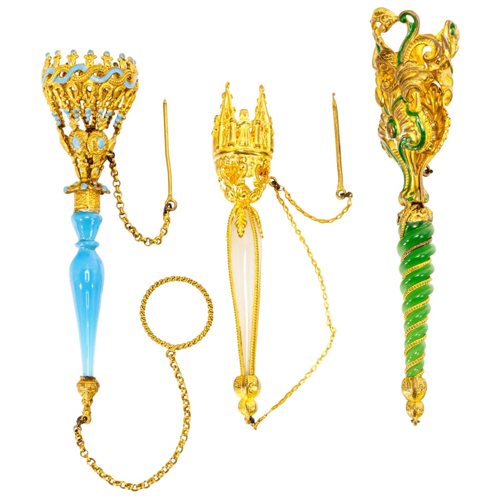 Three French metal and opaline glass child's posy holders or tussie mussies: Three French metal and opaline glass child's posy holders or tussie mussies, circa 1870-1880, comprising two with enamel details and one in the Gothic style, between 4"l and 5"l. Provenance: The Colle