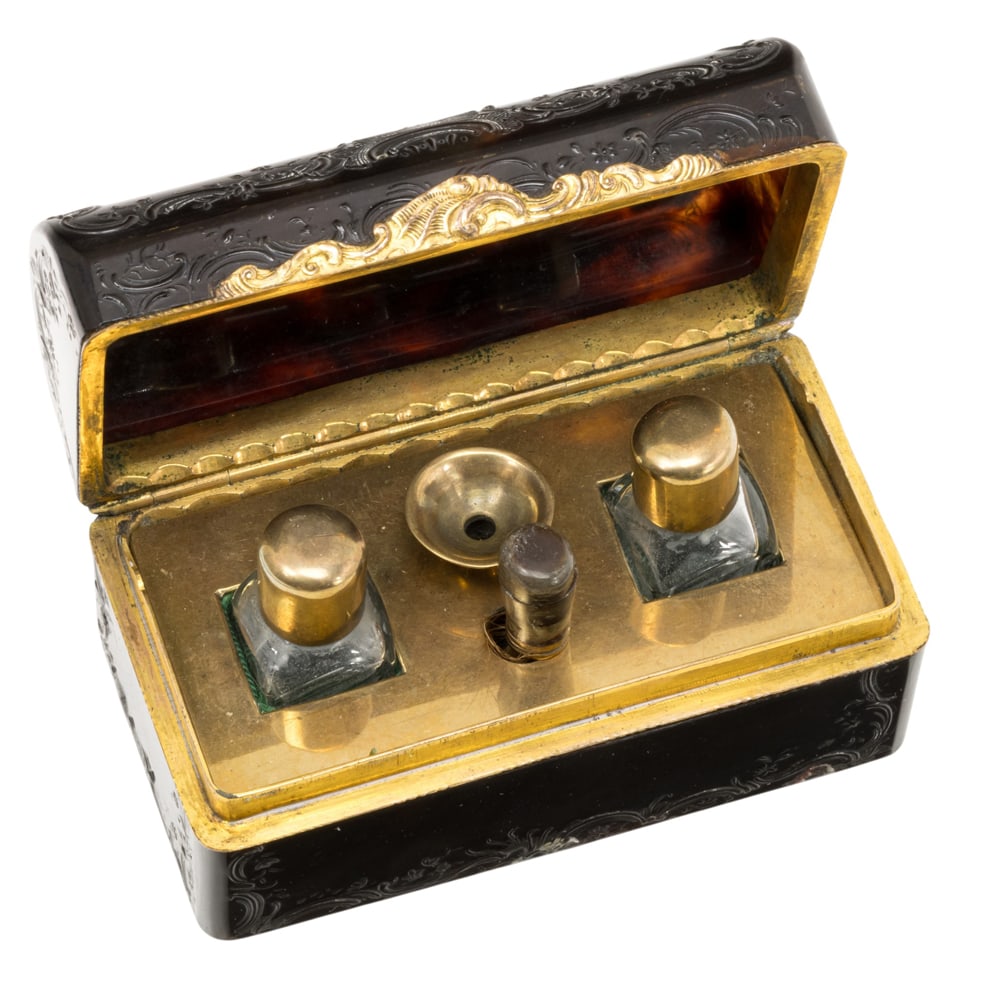 A Napoleon III scent caddy or cave a parfum: A Napoleon III scent caddy or cave a parfum, third quarter 19th century, the domed case decorated with scrolls, the interior fitted with two bottles, funnel and brush, 1.75?h x 3.25?w. Provenance: