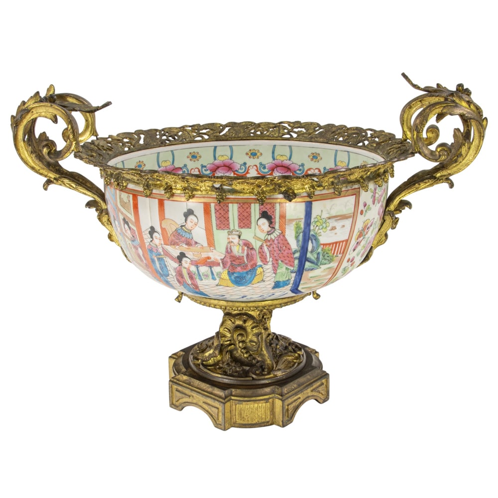 A Louis XV style gilt bronze mounted famille rose porcelain pedestal bowl: A Louis XV style gilt bronze mounted famille rose porcelain pedestal bowl, late 19th century, the bowl painted with scenes of social life and courtiers, within reticulated frame flanked by scrolled ha