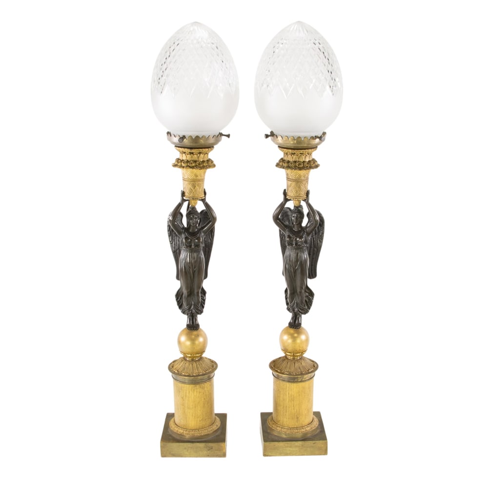 A pair of Louis Philippe patinated and gilt bronze candleabra bases now mounted as table lamps: A pair of Louis Philippe patinated and gilt bronze candleabra bases now mounted as table lamps, mid 19th century, each modeled as a winged beauty holding aloft a flower basket and later fitted with cu