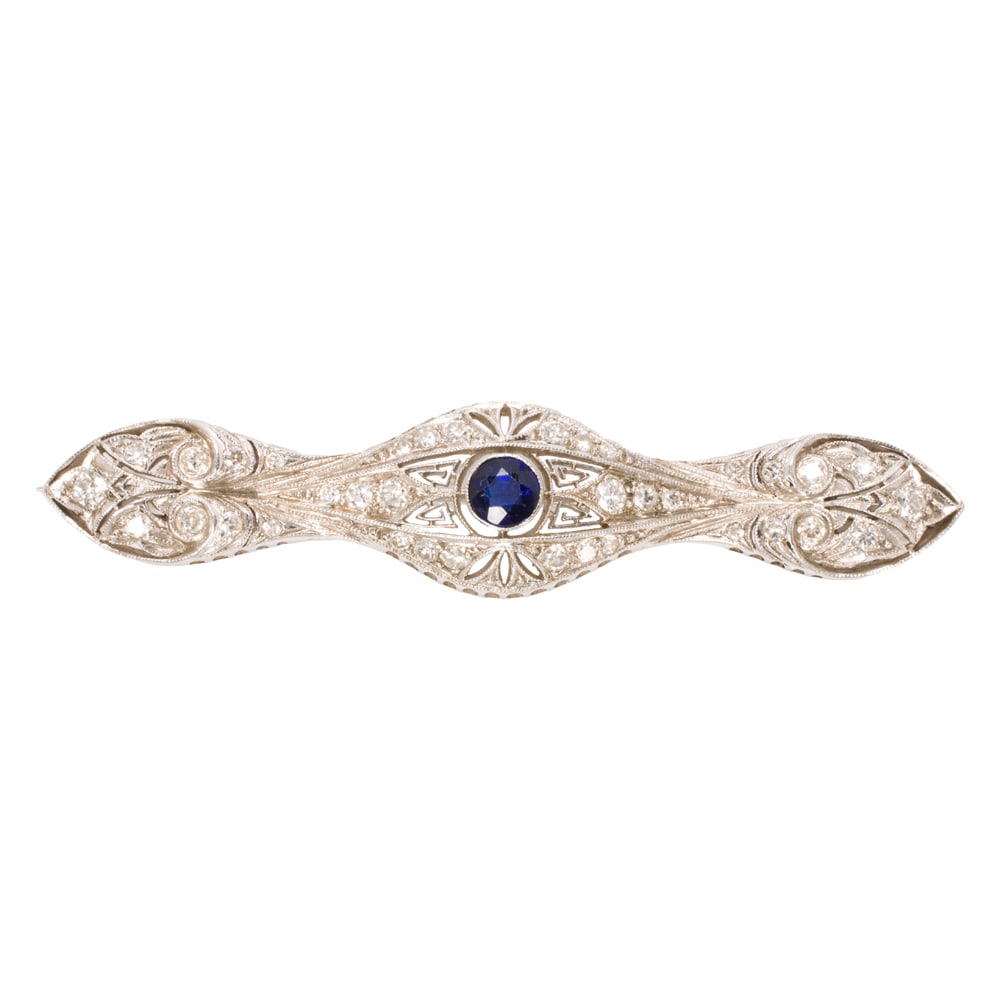An Art Deco style sapphire, diamond, and platinum pin: An Art Deco style sapphire, diamond, and platinum pin Centering a round-cut sapphire weighing approximately 0.50 carat, accented by numerous old mine-cut and round brilliant-cut diamonds weighing appr