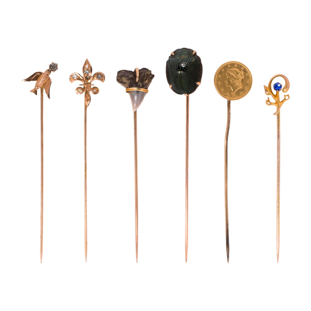 Six gold stick pins: Six gold stick pins Comprising one 10k gold pin, four 14k gold pins, and one 1852 liberty gold dollar set on gold-filled stem; gross weight: 7.75 grams