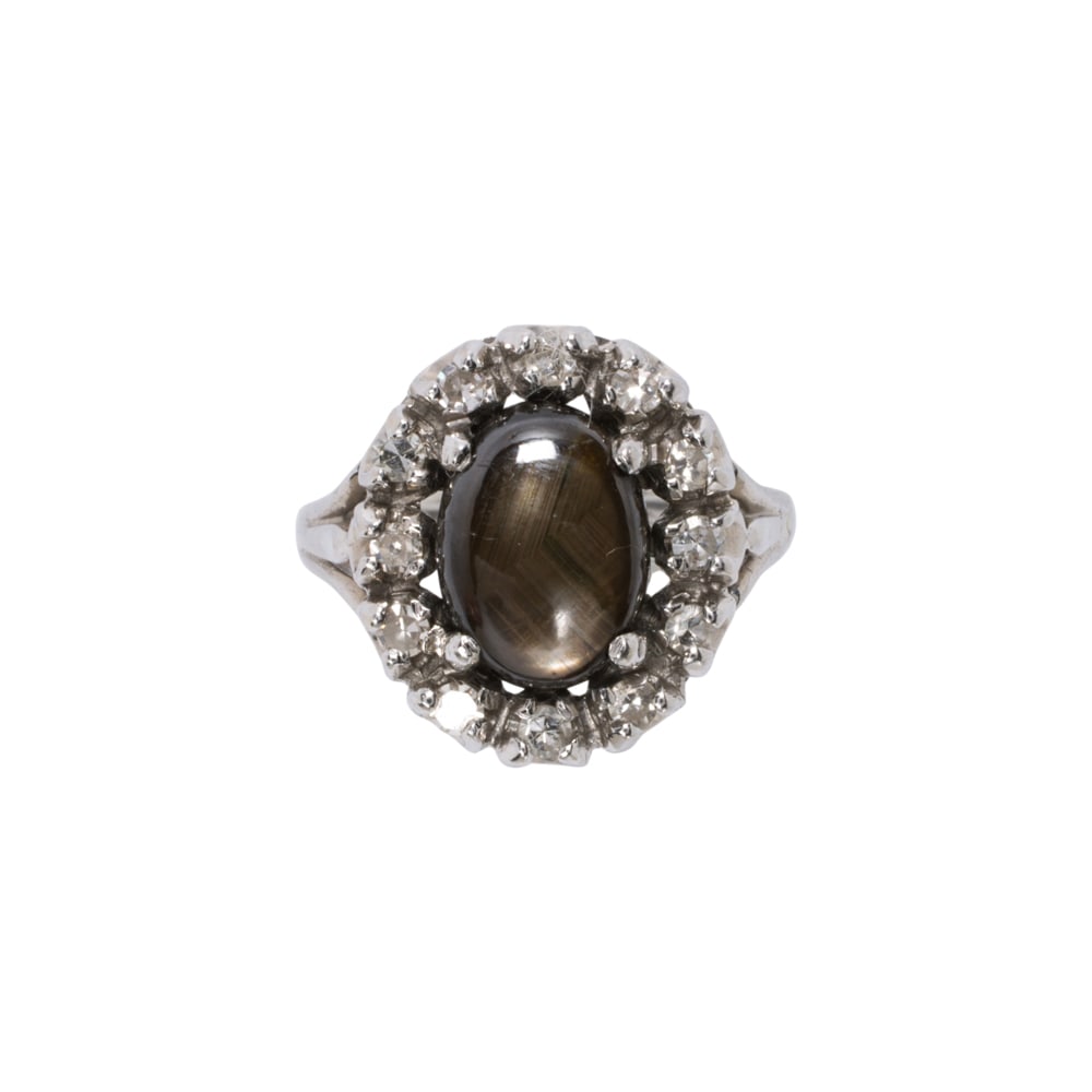 A star sapphire, diamond, and 14k white gold ring: A star sapphire, diamond, and 14k white gold ring Centering an oval-shaped star sapphire cabochon measuring 8.88 x 6.53 x 4.29 mm, framed within a halo of 12 single-cut diamonds; size 2 3/4; 3.35