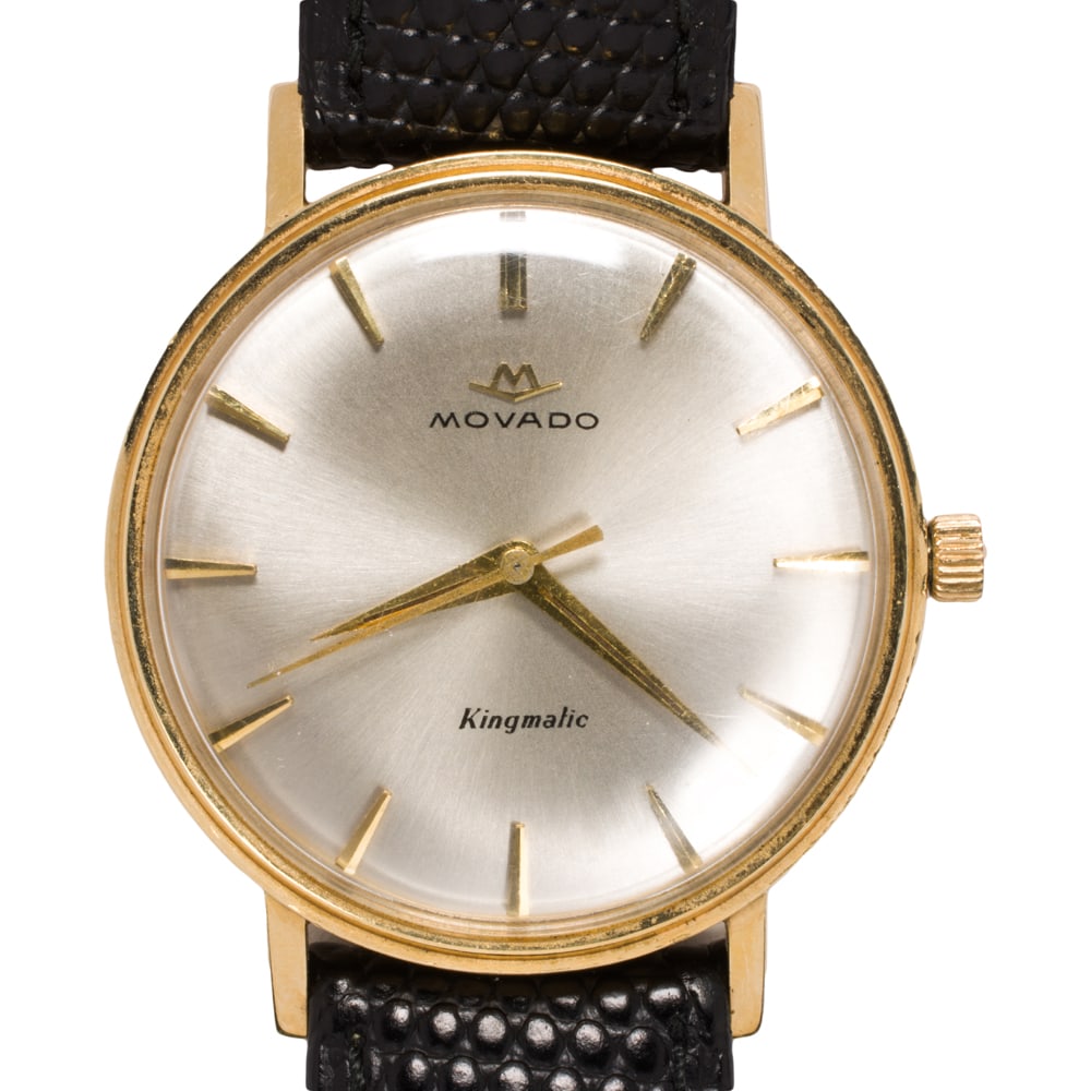 A Movado Kingmatic 14k gold watch: A Movado Kingmatic 14k gold watch The champagne tone face, gold stick indices, gold dauphine hands, within polished 14k gold case, containing a 28 jewels manual movement, on black leather strap; case 