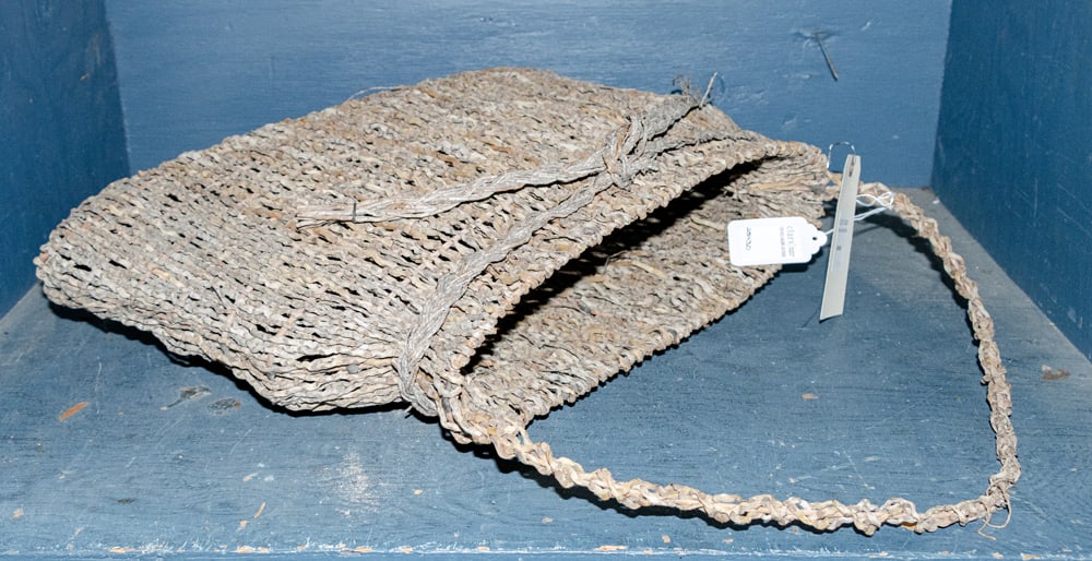 A contemporary handmade basket: A contemporary handmade basket, the natural fiber woven in narrow bag shape and tied with a ribbon, 23" x 22" x 7"