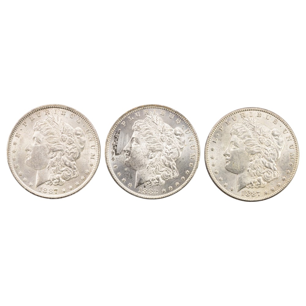 Three Morgan silver dollars: Three Morgan silver dollars, comprising (1) 1882 with reverse toning and (2) 1887 examples, all BU