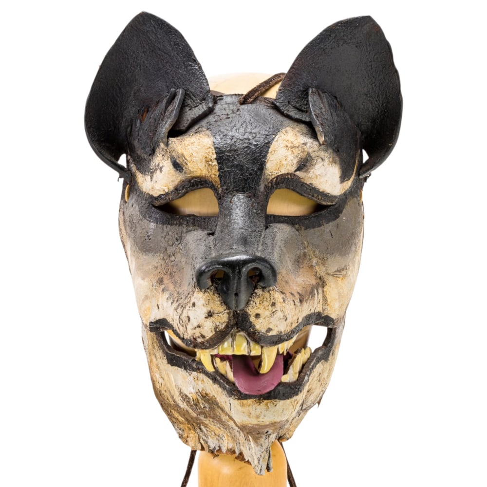 A Folk Art painted leather articulated wolf's mask: A Folk Art painted leather articulated wolf's mask, raised on associated wood stand, mask 12"h x 9"w; overall 21"h
