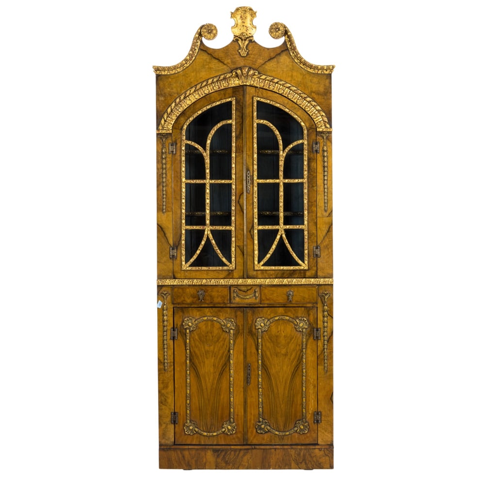An Italian partial gilt olive wood corner vitrine in two parts: An Italian partial gilt olive wood corner vitrine in two parts, first half 19th century, the two glazed doors opening to reverse serpentine fixed shelves resting on the lower case with gilt