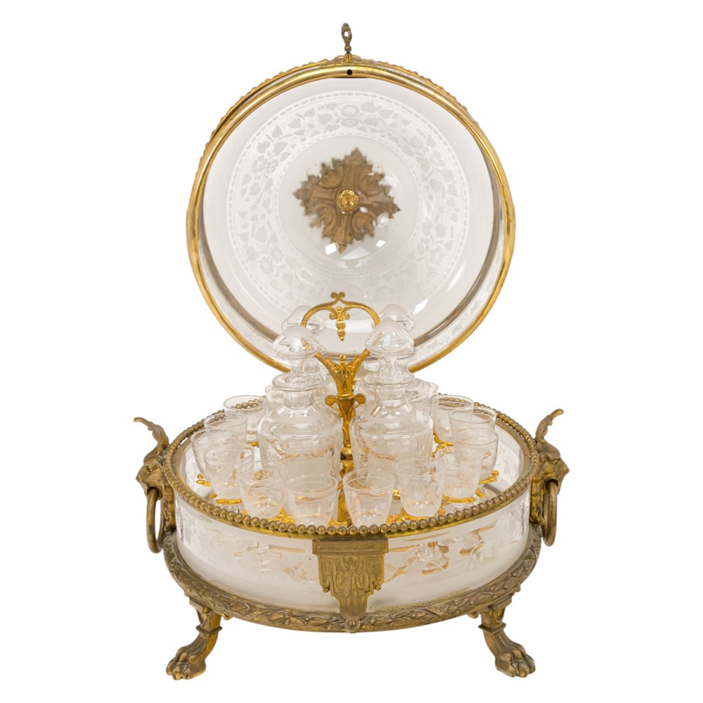 A Baccarat style gilt bronze and engraved glass tantalus: A Baccarat style gilt bronze and engraved glass tantalus, the domed case with floral engraved bands and flanked by lion mask handles, opening to removable rack fitted with four decanters and sixteen