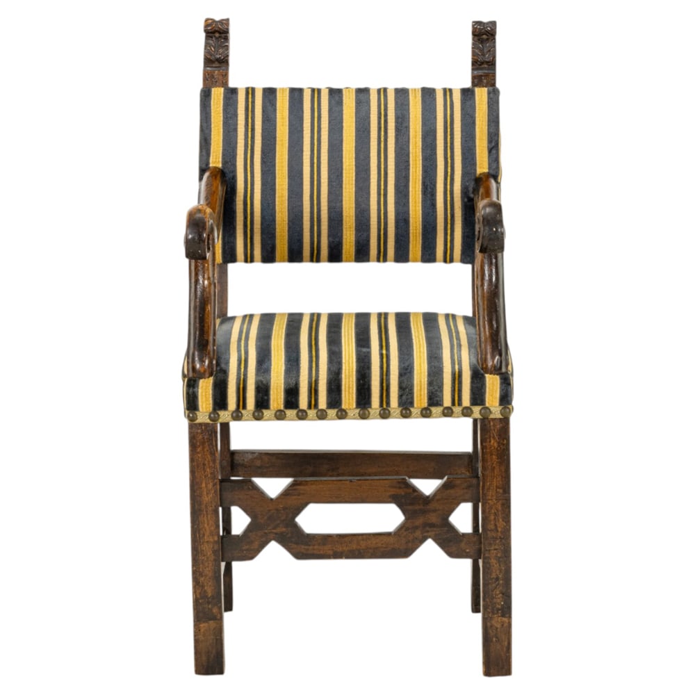 A Spanish Colonial armchair: A Spanish Colonial armchair, with carved finials centering the padded seat and back with striped upholstery and brass nail head trim, having a geometric decorated front stretcher, and rising on