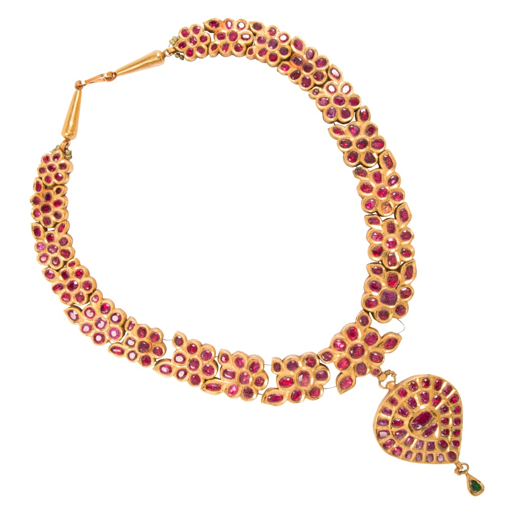 A ruby, emerald, and high karat gold necklace: A ruby, emerald, and high karat gold necklace Of South Asian floriform design, set with numerous foil-backed rubies and one faceted emerald; length: 15 in; 164.35 grams