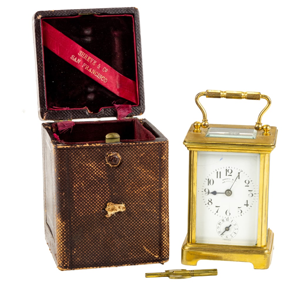 A French gilt brass and glass alarm carriage clock retailed by Shreve & Co.: A French gilt brass and glass alarm carriage clock retailed by Shreve & Co., San Francisco, the Corniche style case with fitted carrying case, clock: 4.5"h x 3"w x 2.3/4"d (excluding handle)