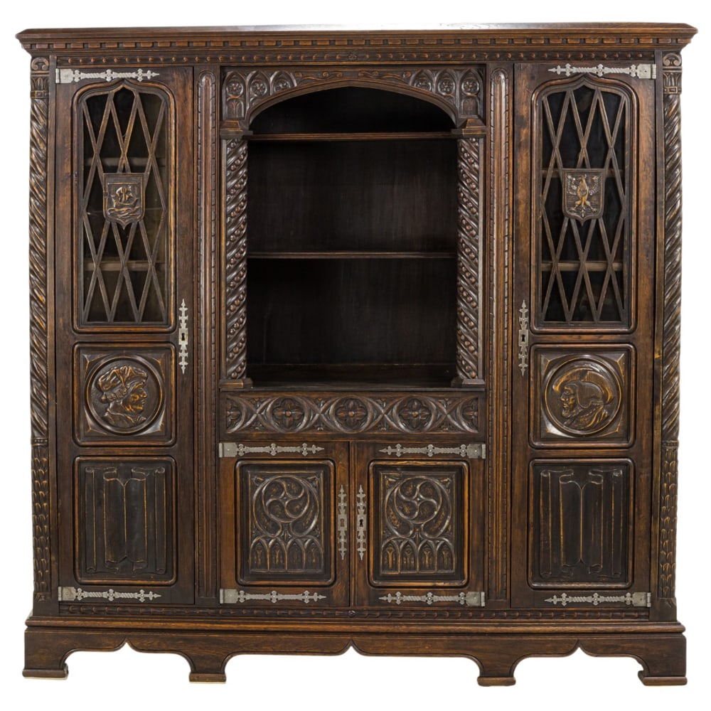 A Spanish Revival oak cabinet: A Spanish Revival oak cabinet, with relief carved panels flanking the doors retaining strap hinges, the case with carved pilasters, and rising on bracket feet, , 68.5"h 69.5"w x 17"d