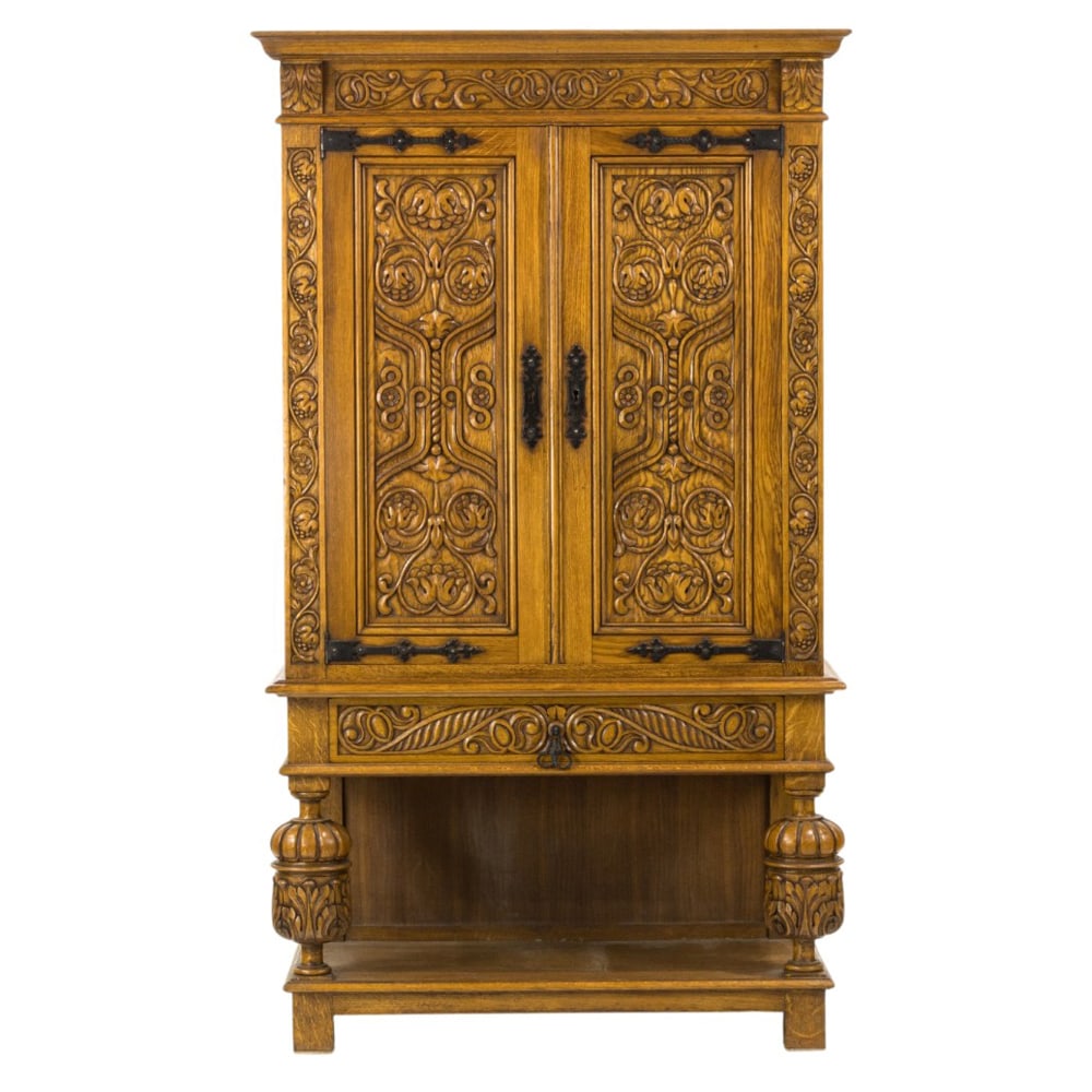 A Spanish Revival carved cabinet: A Spanish Revival carved cabinet, the two door case with carved vine and leaf reserves, strap hinges, and cup and urn supports, overall 67.5"h x 39"w x 19.5"d