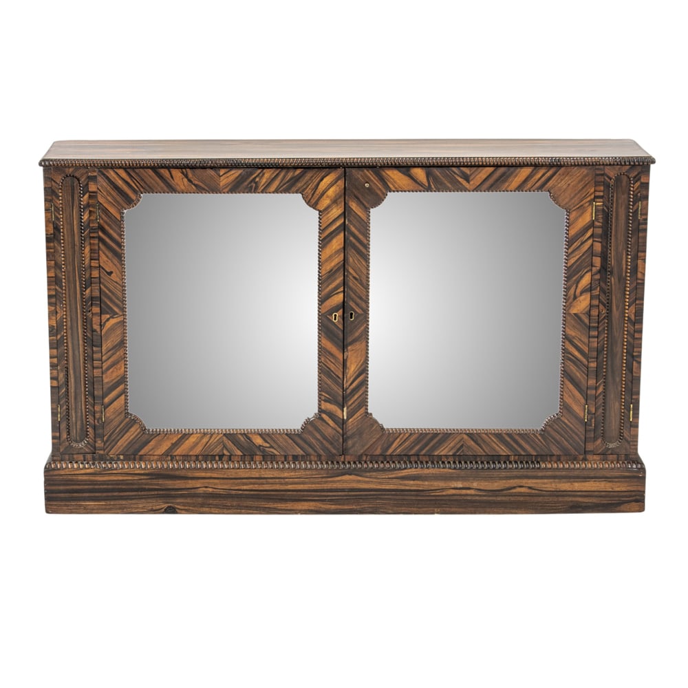 A Regency highly figured coromandel veneer sideboard: A Regency highly figured coromandel veneer sideboard, early 19th century, the two mirrored doors opening to adjustable shelves, the case with carved edges, and rising on a molded base, 35"h x 60"w