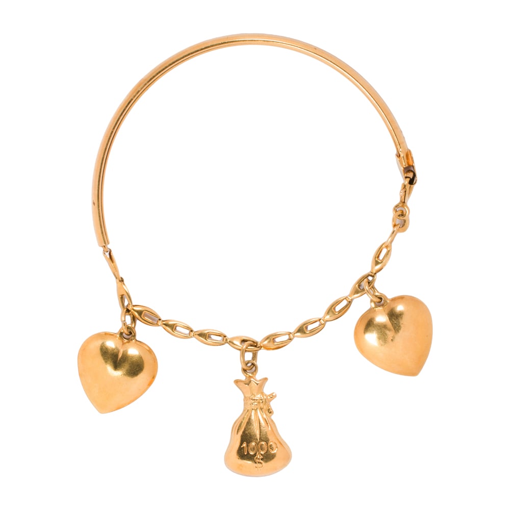 An 18k gold charm bracelet: An 18k gold charm bracelet The half-bangle charm bracelet featuring three heart and money bag charms; length: 7 1/2 in; 12.30 grams