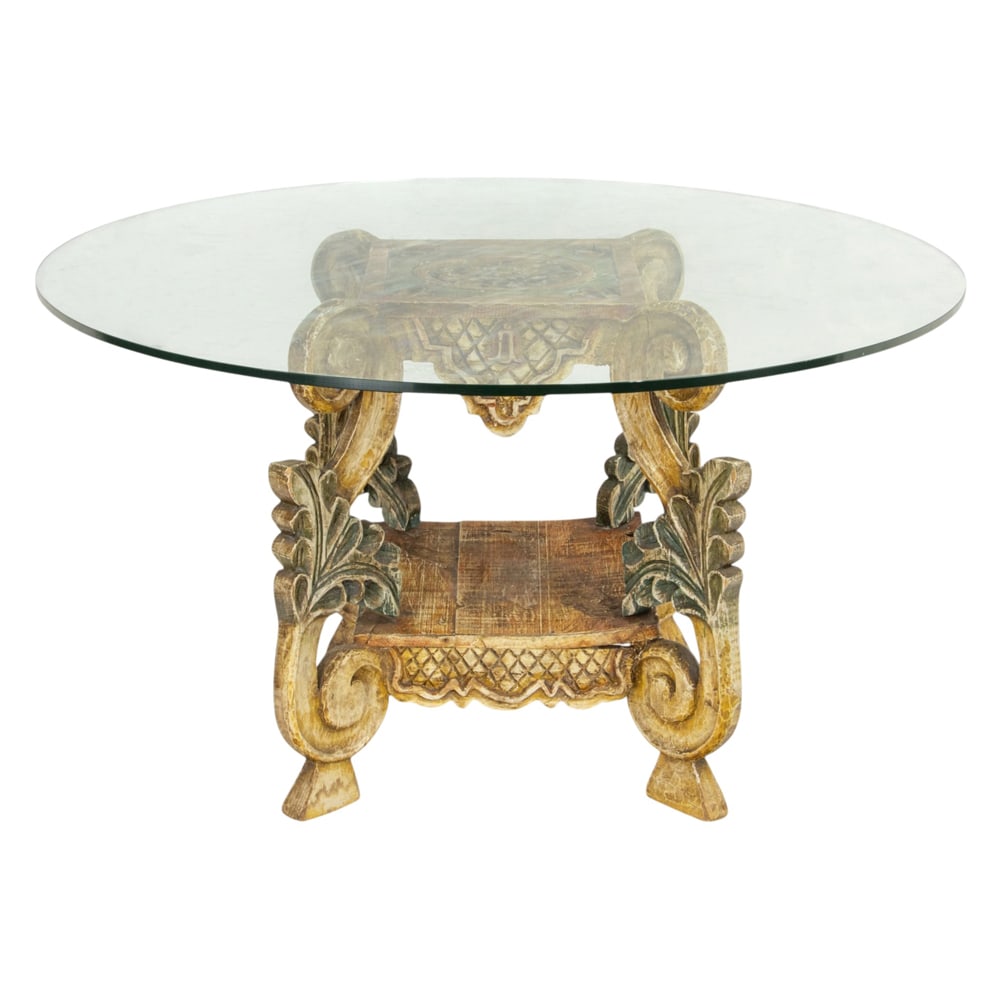 A Southwest carved and polychrome decorated dining table: A Southwest carved and polychrome decorated dining table, the glass top above the acanthus decorated supports conjoined by the lower tier, 29"h x 45"dia