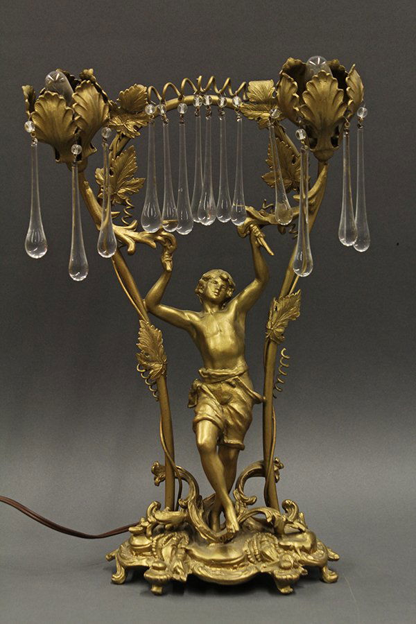 Art Nouveau style figural gilt metal lamp: Art Nouveau style figural table lamp, the playful boy depicted under a canopy of gilt metal foliage flanking the two lights accented with crystal rain drops, rising on a Rococo style base, 16"h x 10"w