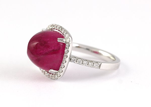 Pink tourmaline diamond white gold halo style mounted: Pink tourmaline, diamond and 18K white gold ring centering one sugar loaf cabochon pink tourmaline measuring approximately 12.0 x 11.75 mm, weighing approximately 10.69 cts., numerous full cut diamond