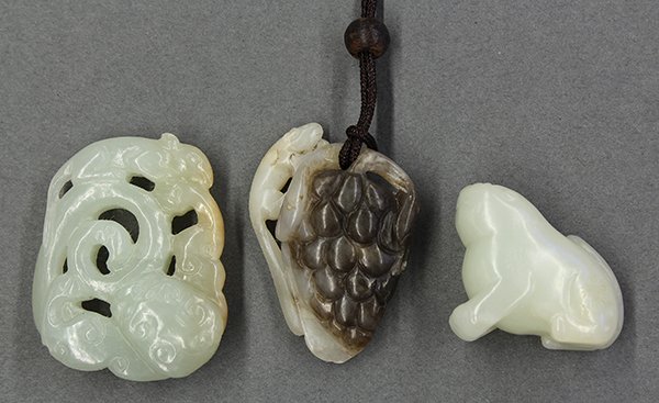 Chinese Jade Carvings: Lion, Grape, Squirrel: (lot of 3) Chinese jade toggles: the first of a seated humorous fu-lion of celadon hue; second, a toggle with a cluster of grapes executed from the dark gray matrix in contrast with the squirrel of li