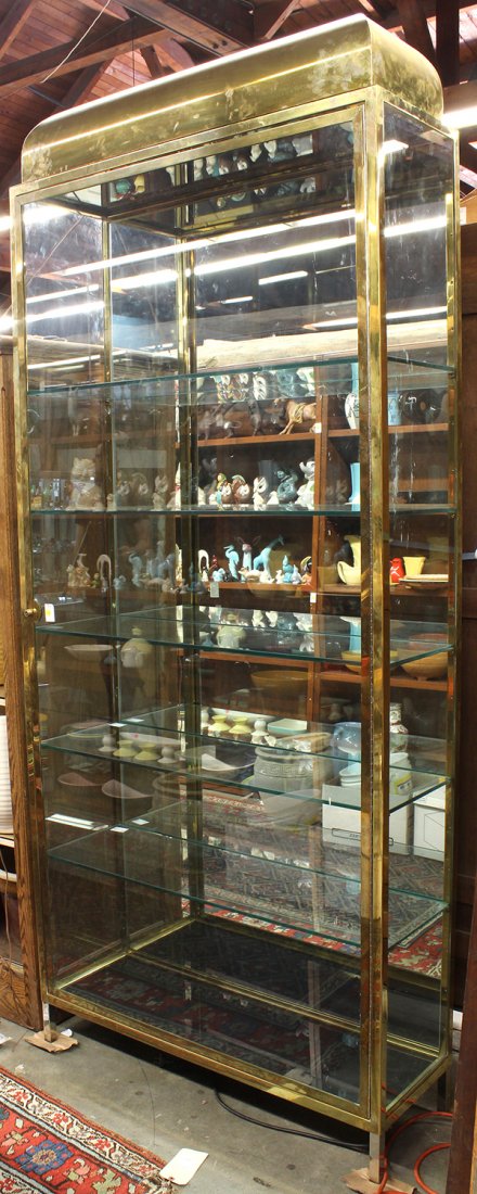Moderne brass and glass vitrine,: Moderne brass and glass vitrine, of rectilinear form with a brass frame, the single glass door opening to glass shelves, and rising on square chrome feet, 97"h x 42"w x 14"d.