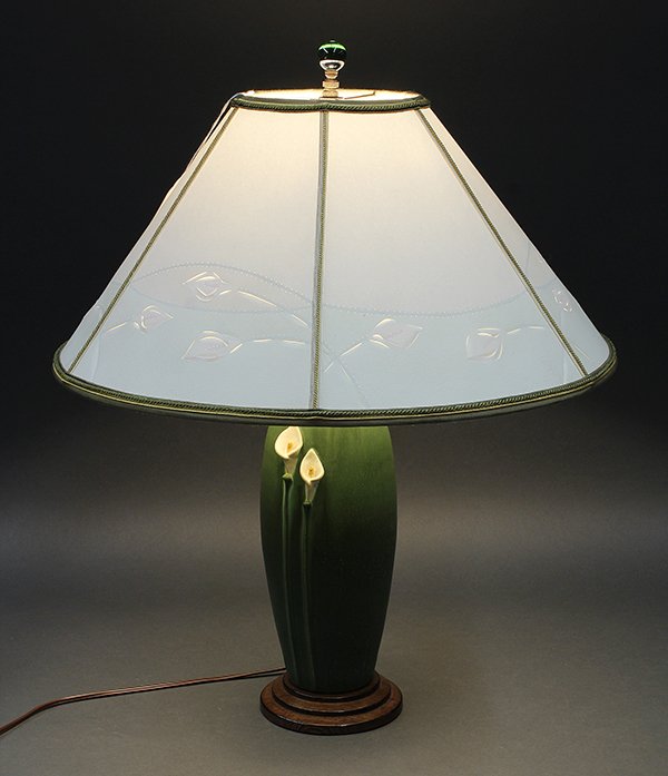 Arts and Crafts Ephraim faience pottery table lamp: Arts and Crafts Ephraim Faience pottery table lamp, having a cut-paper lily lamp shade, above the pottery base having lily decoration on a green ground, and rising on a graduated circular base, 23"h o