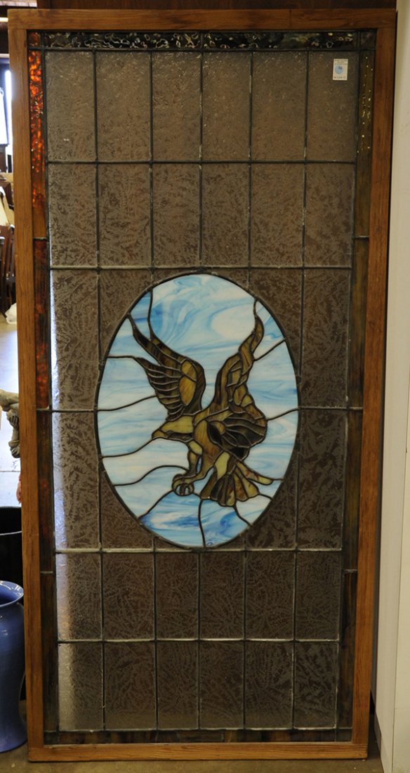 Oak framed leaded and stained glass window: Oak framed window having leaded, frosted, and textured glass panels, surrounding a central reserve of blue and brown slag glass depicting an eagle in flight, 70"h x 34"w x 1.5"d Note: Sold on behalf o