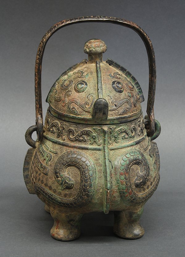 Chinese Archaistic Bronze You Vessel: Chinese archaistic bronze handled wine vessel (you), the domed lid with taotie masks, above the body cast with mythical creatures of a serpent form and raised on four supports, the separate handle wit