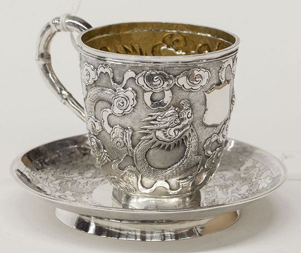 (lot of 2) Chinese Export silver teacup and saucer: (lot of 2) Chinese Export silver teacup and saucer, by Wang Hing & Co., Hong Kong, late 19th century, the cup decorated with a chased repoussé writhing dragon amidst clouds against a finely hammered