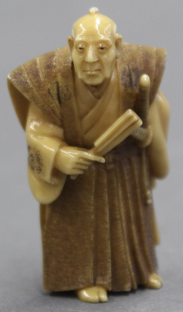 Japanese Ivory Netsuke Samurai: Japanese ivory netsuke, a feudal retainer wearing two katana, holding a fan and a shrine register book behind his back, marked 'Dosei', 2"h