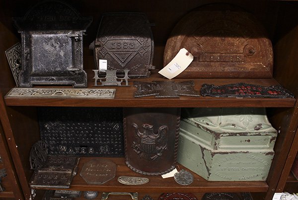 Three shelves of cast iron architectural elements: (lot of 31) Three shelves of cast iron architectural elements, including stove doors and tops, door knob back plates, handles, and a fragment of a Victorian column base from Oakland, Ca, 14"h x 18"w. 