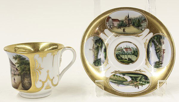 KPM scenic porcelain cup and saucer: KPM scenic porcelain cup and saucer, mid 19th century, the cup having thick gold rim leading part way into the interior and a hand painted scene of a village scene along a boulevard amongst gracious h