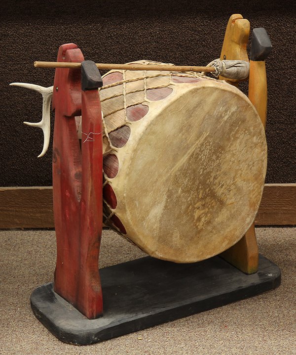 Plains paint decorated hide and carved wood drum on: Plains paint decorated hide and carved wood drum on stand, the suspended drum with pigment accents centering the figural carved supports decorated with hand carved antlers and rising on an ebonized ba