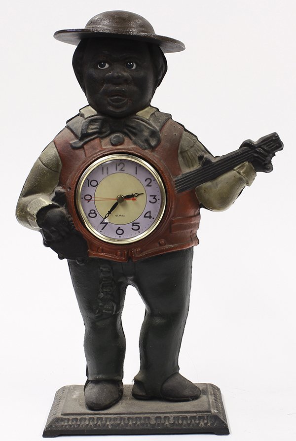 Black Americana cast iron figural clock, depicting an: Black Americana cast iron figural clock, depicting an African American minstrel holding a banjo, the drum of which holds the battery operated clock face, resting on a rectangular plinth, 15.5"h