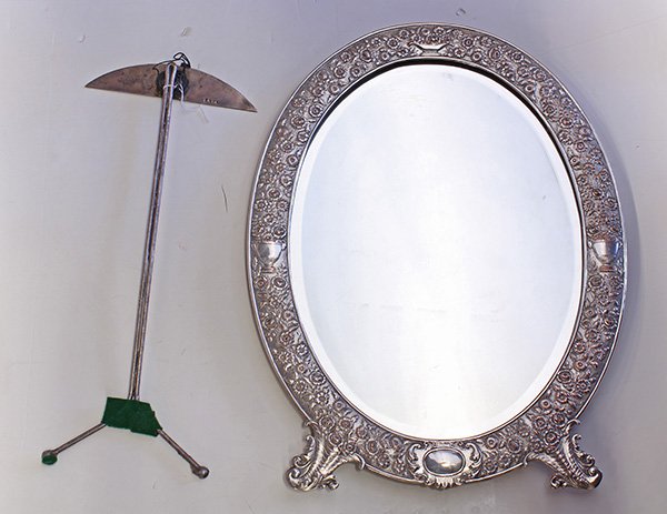Oval silverplate counter top mirror: Oval silverplate counter top mirror, having a repousse floral frame with outswept feet and beveled glass; 21"h x 16"w