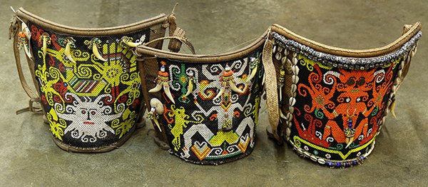 (lot of 3) Indonesian tribal baby carriers, executed in: (lot of 3) Indonesian tribal baby carriers, executed in beaded basketry, possibly Dayak, each of demilune form with an intricately beaded panel depicting mythological beings, trimed with cowrie shells