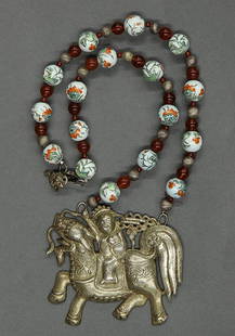 Chinese Necklace with Silver Plaque: Chinese silver plaque with bead necklace, featuring a repousse plaque with a child mounted on a qilin, stranded to a necklace with porcelain, carnelian and silvered beads, 15.5"h