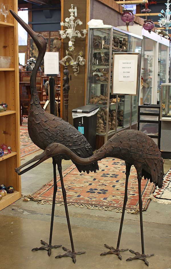 Two Metal Cranes: Pair of metal sculptures of cranes, one looking upward, and the other with neck lowered and a fish in its beak, 56.75"h. Provenance: From the estate of Edward Gerber