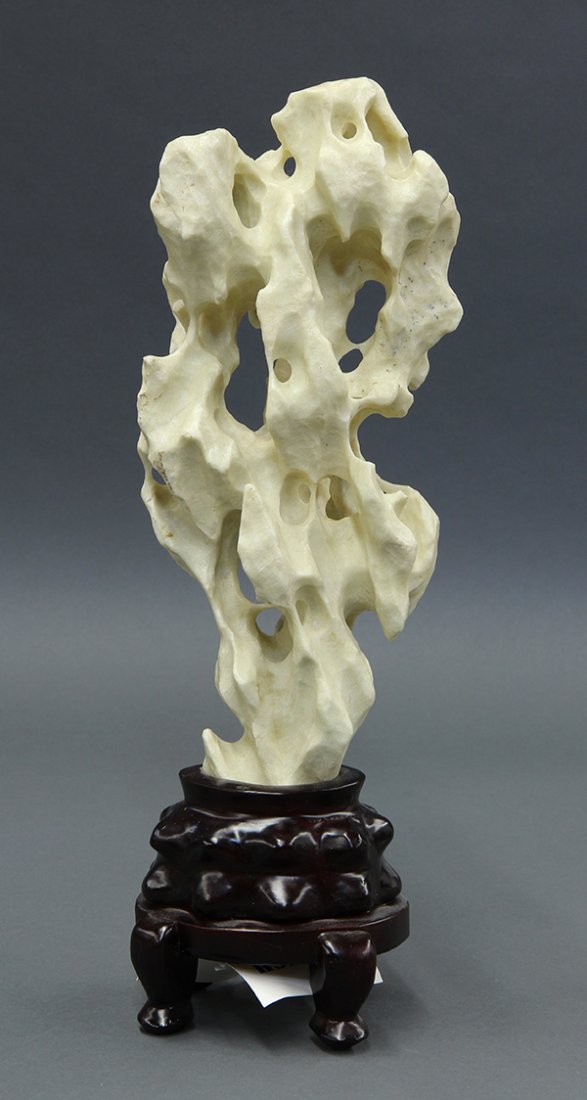 Chinese Taihu-style Small Scholar's Rock: Chinese Taihu-style scholar's rock, the vertical structure with a tapering base and various grottoes, with wood stand, approximately 12"h. Provenance: From the estate of Edward Gerber