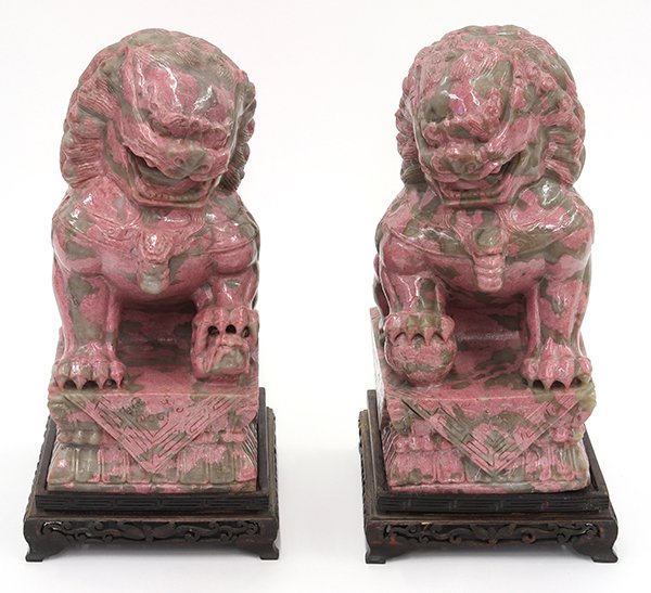 Chinese Rhodonite Fu Lions: Pair of Chinese rhodonite carvings of fu lions, seated on their haunches above a plinth, with wood stands, 9.5"h. Provenance: From the estate of Edward Gerber