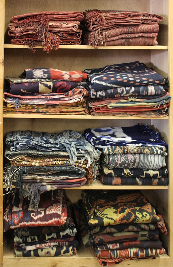 Four shelves of ethnographic textiles: Four shelves of ethnographic textiles, consisting of hand woven Indonesian Ikats executed in cotton in reds, yellow, and blues, together with several cotton embroideries, of varying sizes. Provenance: