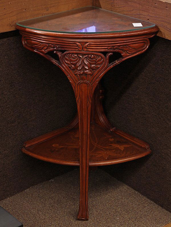 Pair of Art Nouveau style corner tables, each having a: Pair of Art Nouveau style corner tables, each having a glass top above a carved apron, continuing to the lower tier with inlaid foliate decoration, and rising on a single outswept leg, 32"h x 21"w x 1