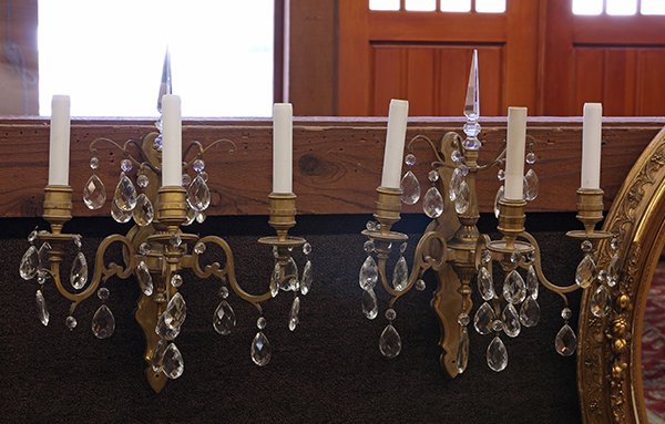 (lot of 4) Continental gilt bronze and crystal wall: (lot of 4) Continental gilt bronze and crystal wall sconces, each three light fixture with prism finial surmounting the reeded standard supporting the three lights accented with crystal drops, (one la