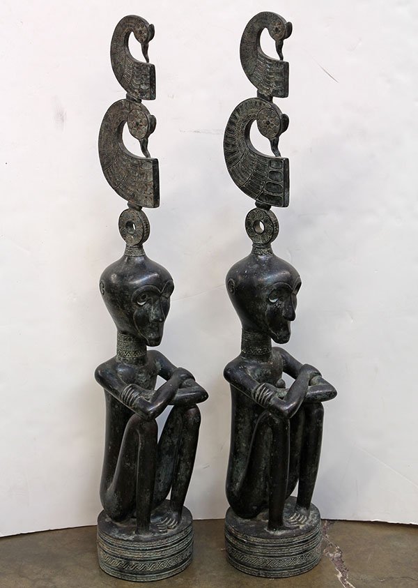 Indonesian metal male and female seated figures with: Pair of Indonesian metal male and female seated figures with arms crossed, and surmounted with a stylized bird head-dress decorated with tribal patterns, 40". Provenance: From the estate of Edward Ger