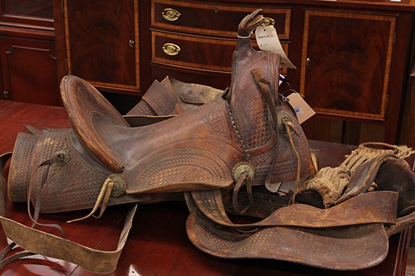 Vintage leather bear trap saddle: Vintage leather bear trap saddle, possibly by the Sternberg Saddlery of Oregon, mostly tooled with silvered conchas, with stirrups, 19"h x 27"w x 17"d