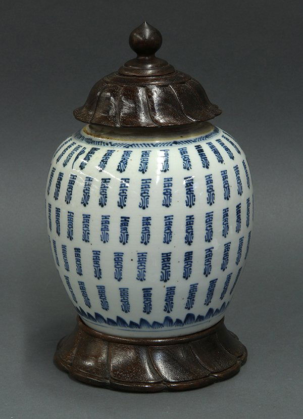 Chinese Blue and White Porcelain Jar: Chinese underglaze blue porcelain jar, the tapered round body repeated with rolls of a stylized Shou script, the base accented with petals and a double ring mark, with wood base and wooden lid (jar dr