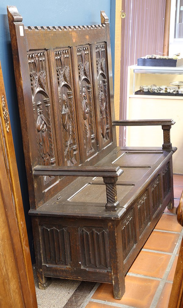 Gothic Revival oak hall settle: Gothic Revival oak hall settle, 19th century, the high back centered with relief carved Ecclesiastical figures surmounted by the trefoil reserve, having a hinged plank seat and rising on rectangular l