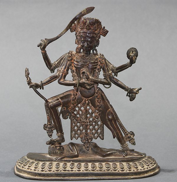 Himalayan Bronze Buddhist Deity: Himalayan bronze figure of a dharmapala, the wrathful deity with six arms holding a sword, trident, disk and head, standing above a body on a lotus pedestal, with traces of red pigment, 6.25"w
